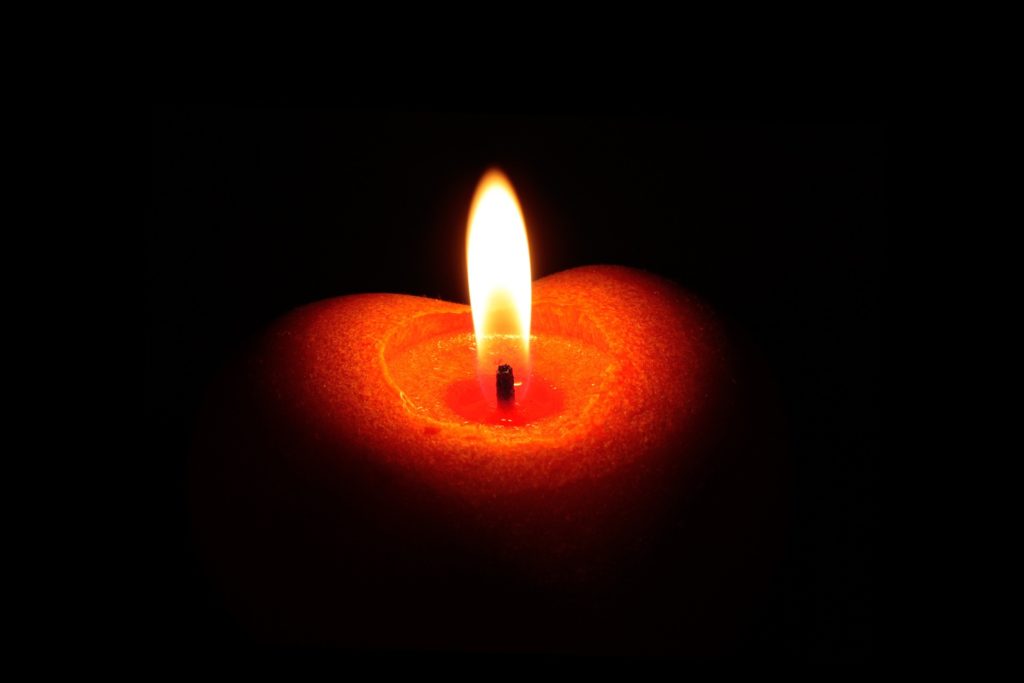 Brennende rote Kerze in Herzform vor schwarzem Hintergrund. 